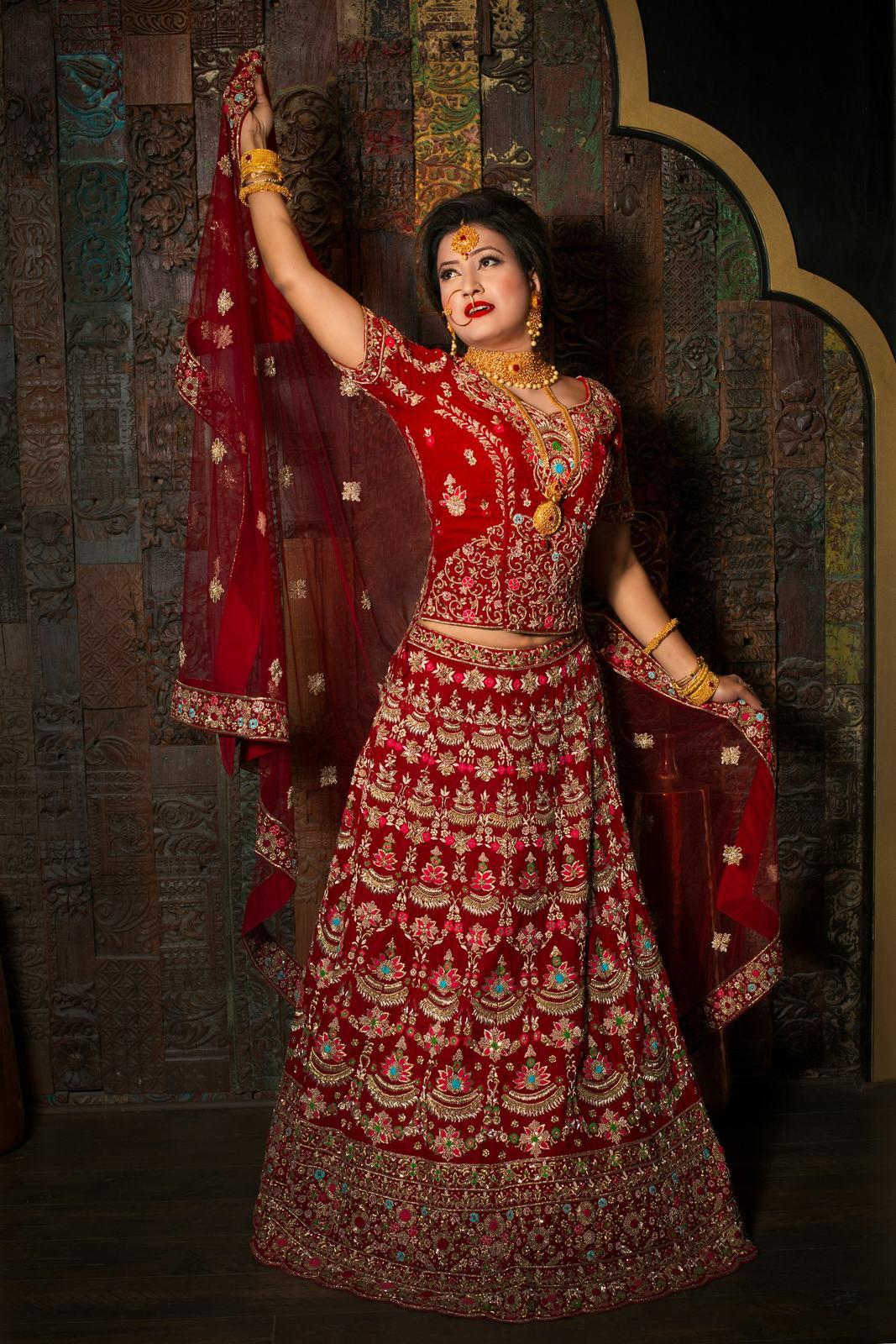 Bride in a red lehenga posing in a carved archway