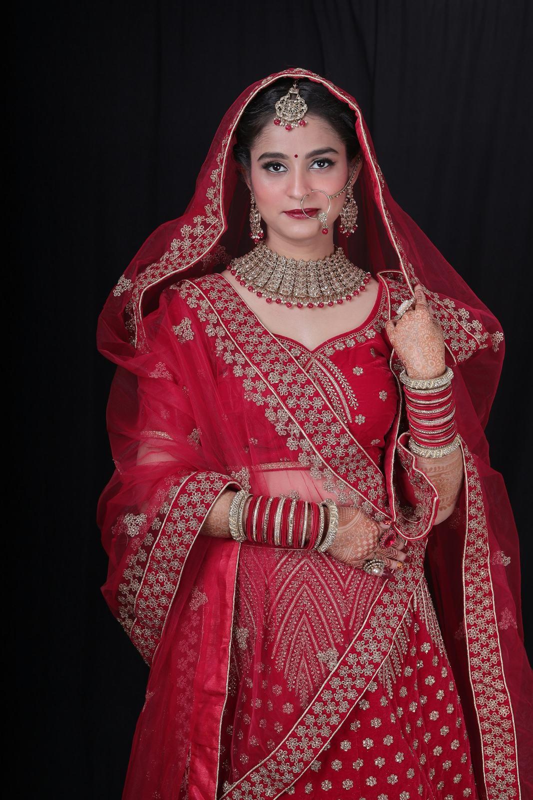 Bride in a red embroidered lehenga against a black backdrop