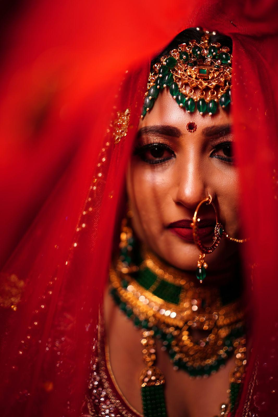Close portrait of a bride under a red veil with kundan jewellery