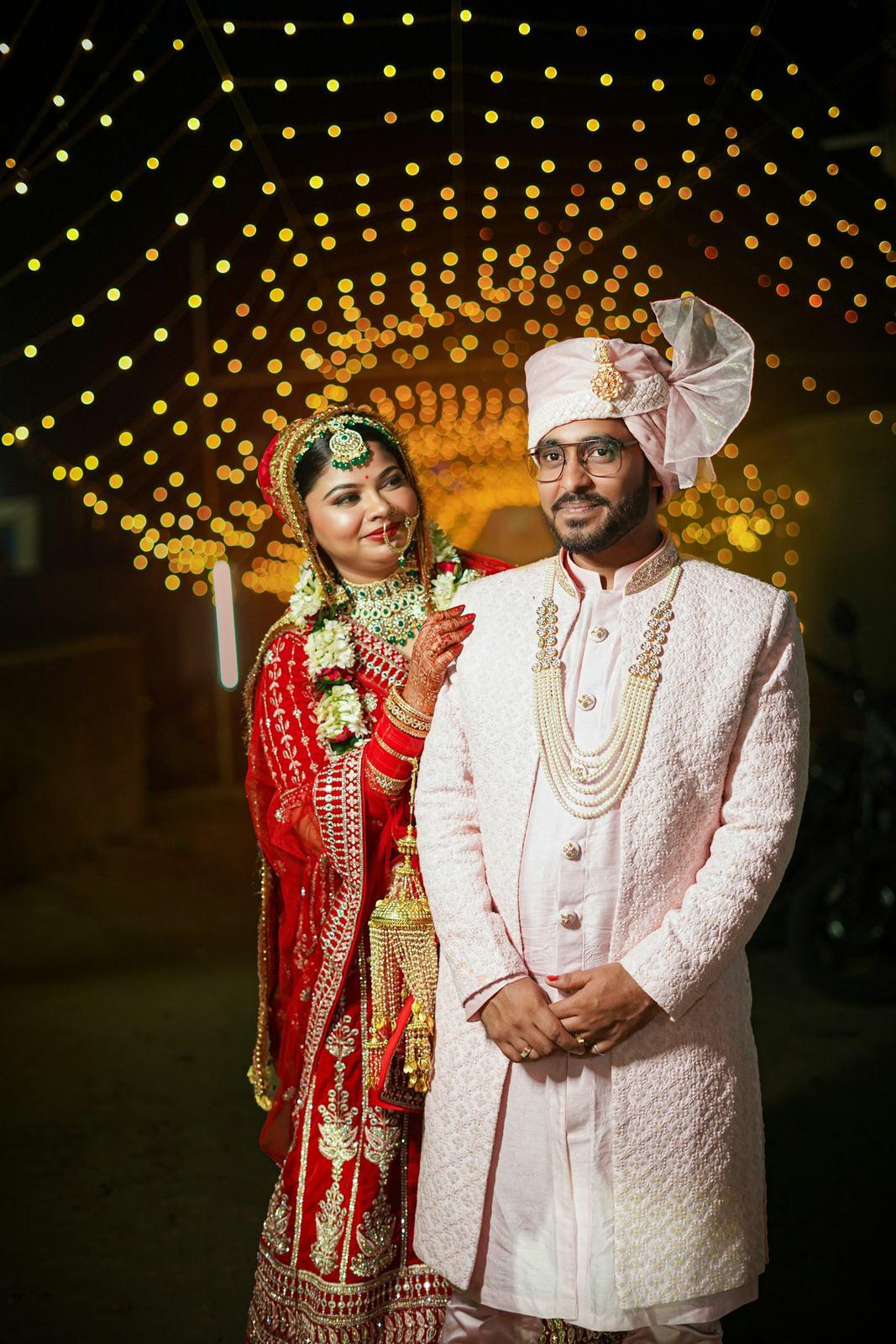 Bride in red and groom in ivory sherwani under string lights