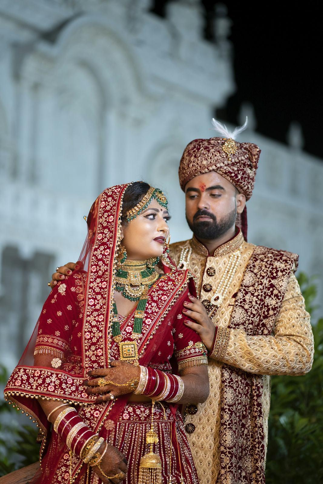 Couple in red and gold wedding clothes in front of a palace