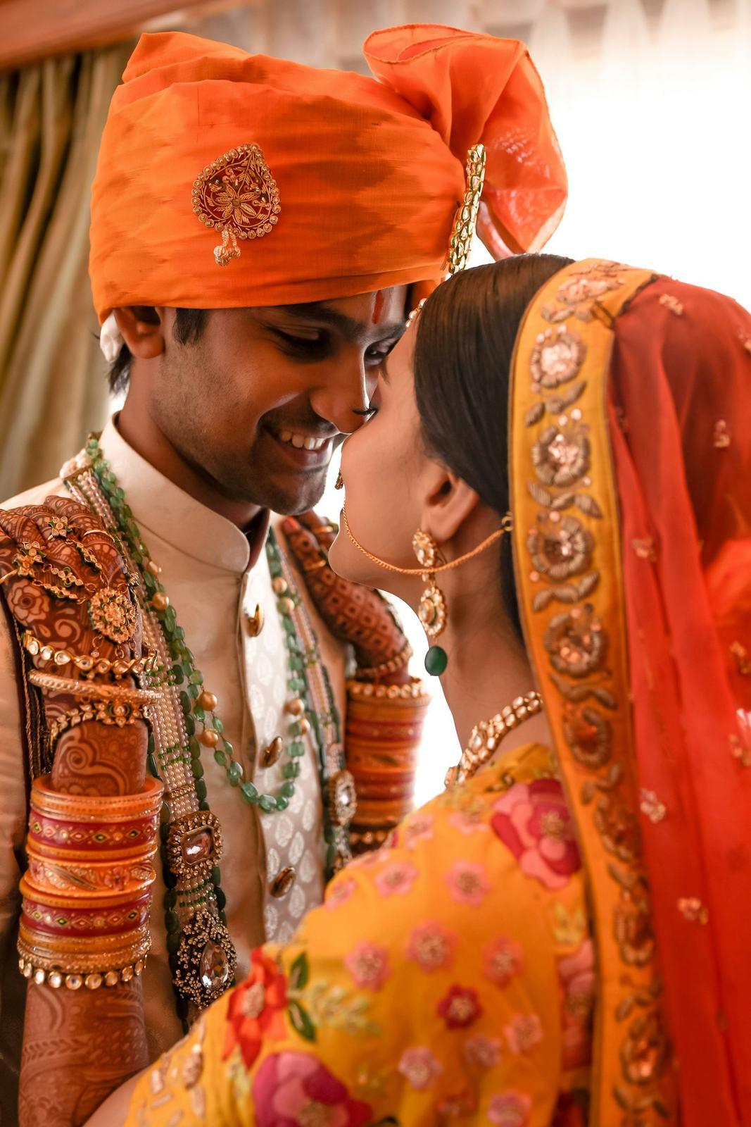 Groom in an orange safa leaning towards the bride