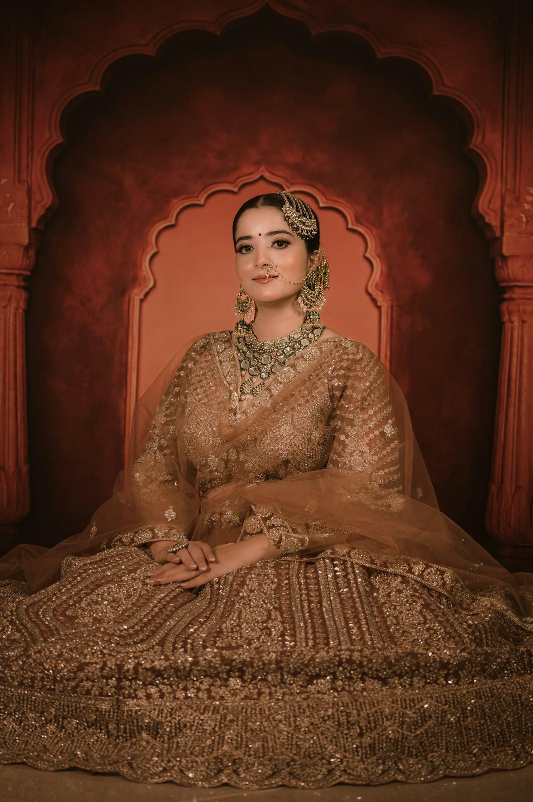 Bride in a gold lehenga seated before a carved red arch