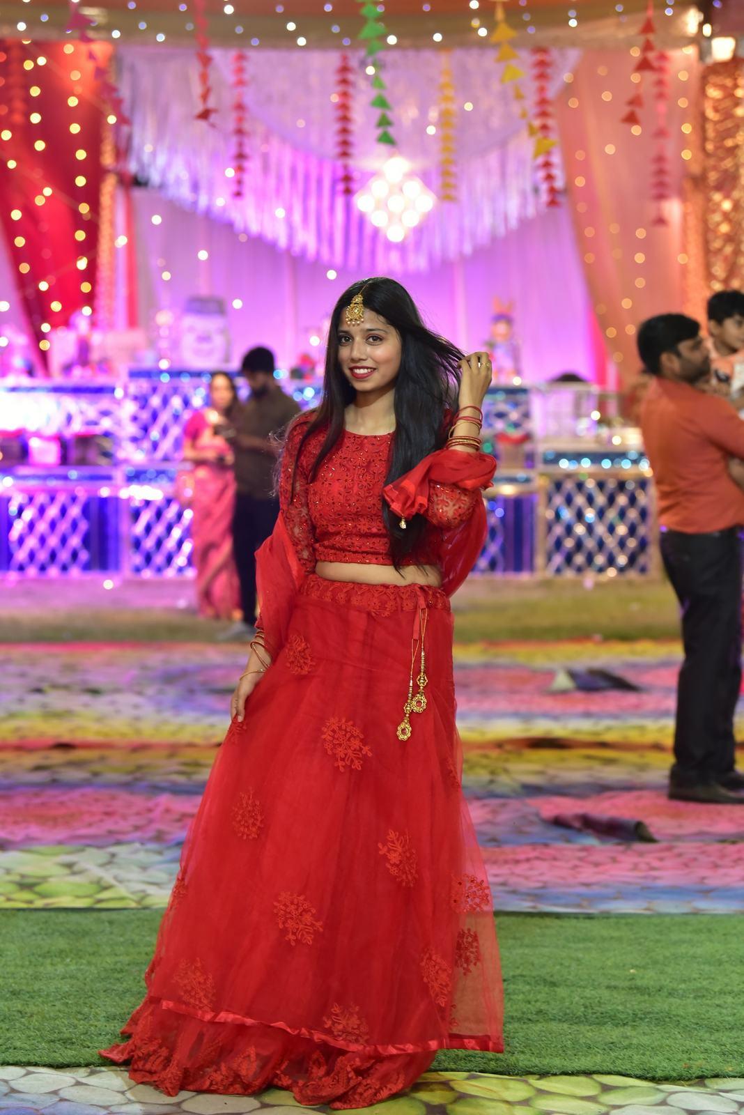 Guest in a red lehenga at a sangeet under pink lights
