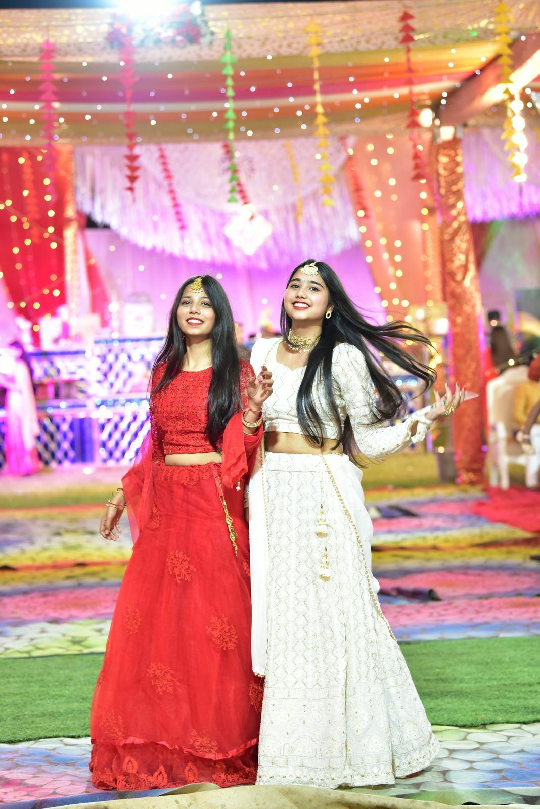 Two friends in red and ivory lehengas at the sangeet