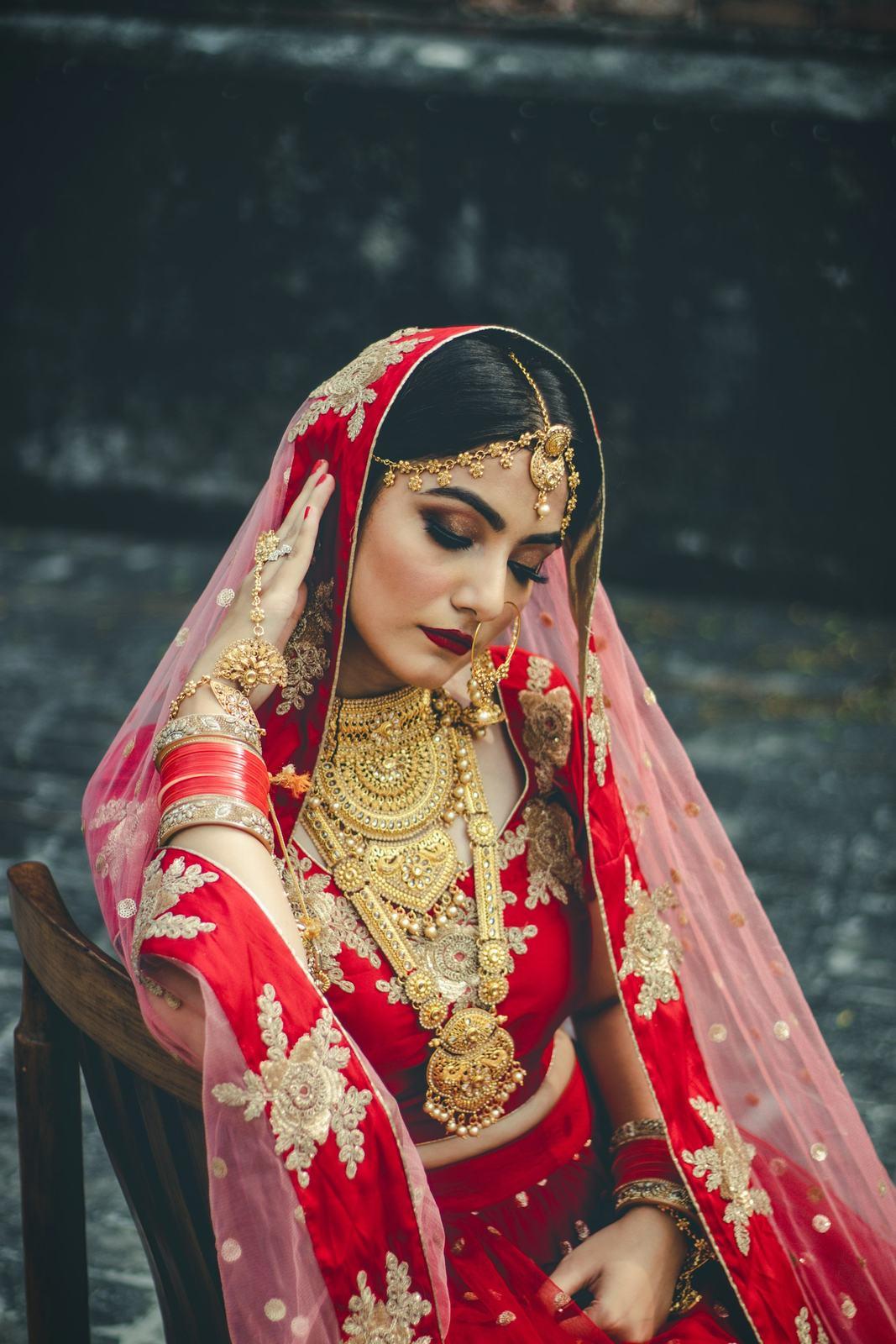 Bride in a red lehenga and gold jewellery seated outdoors