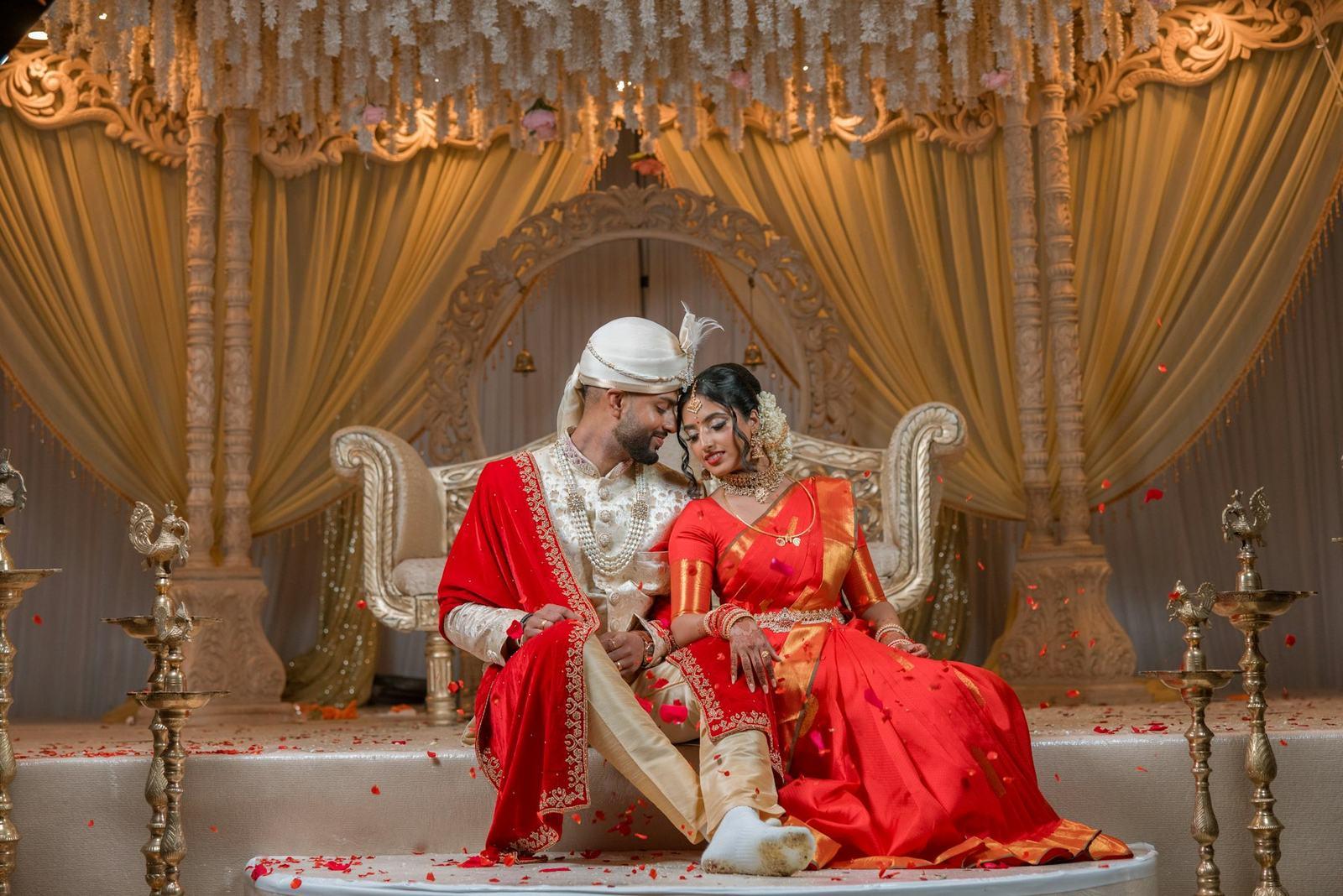 Couple seated together on a carved throne at the mandap