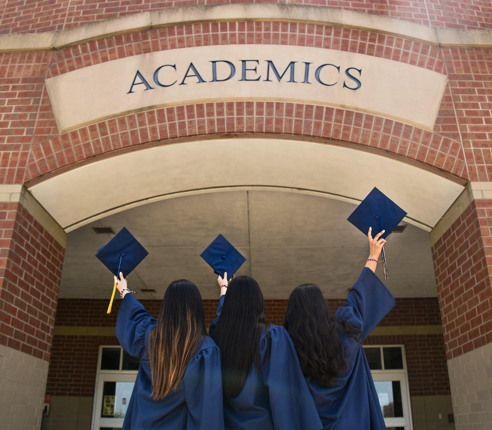 Three graduates raising their caps under a university archway