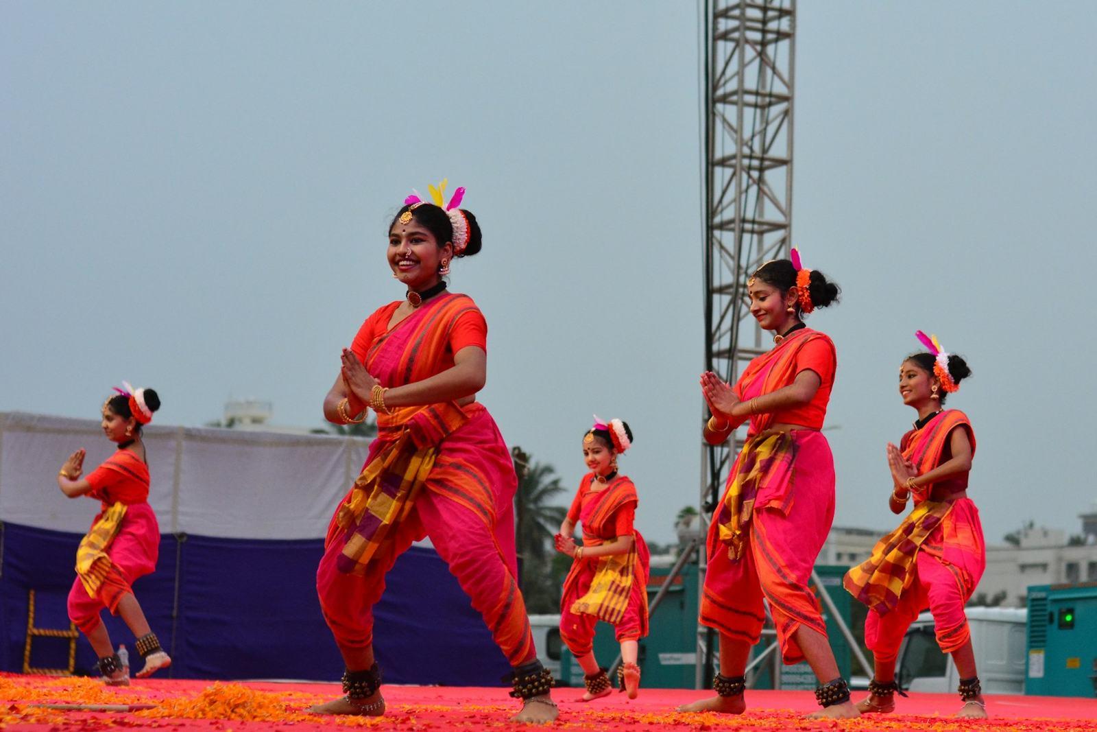 Students in red costumes performing a dance on stage at a school annual day